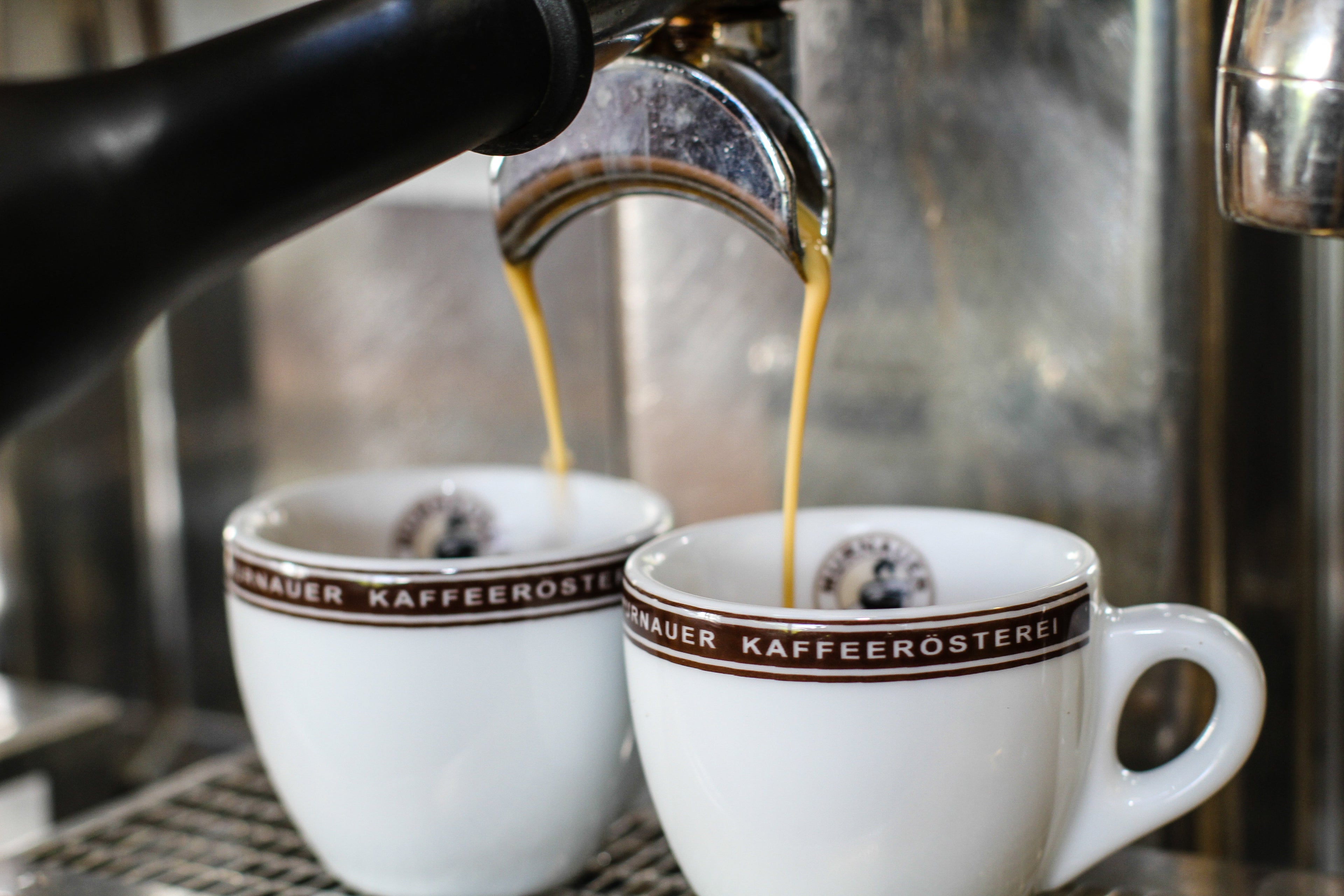 Espressomaschine brüht frischen Espresso in zwei Tassen der Murnauer Kaffeerösterei, goldener Strahl mit entstehender Crema