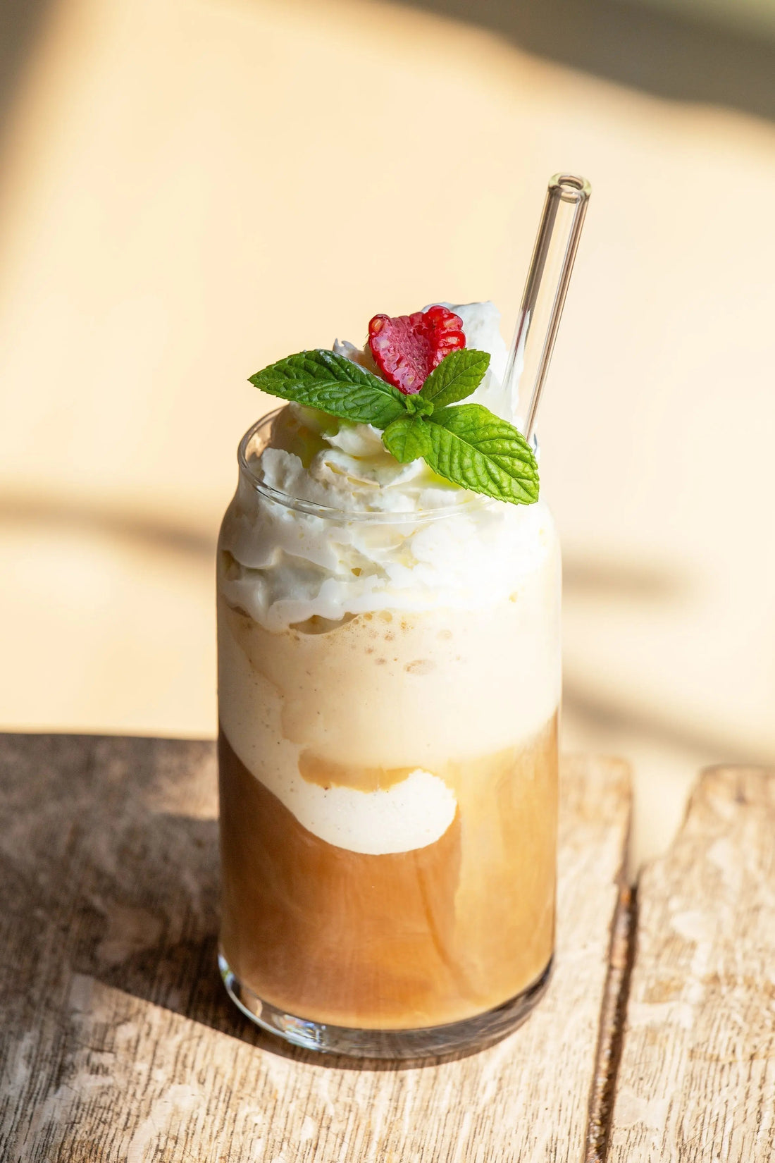 Hoher Eiskaffee Classic on Ice im Glas mit Vanilleeis, Sahnehaube, Minzblatt und Glasstrohhalm auf Holztisch.