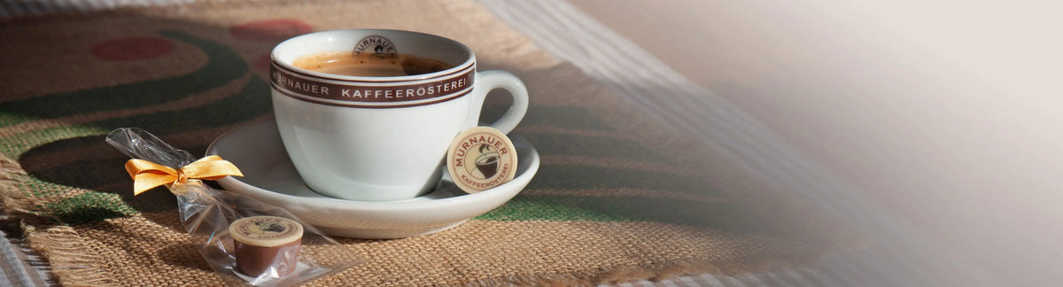 Kaffeetasse der Murnauer Kaffeerösterei auf Jutesack mit eingepackter Praline daneben als Banner für das Kaffee-Gesamtsortiment