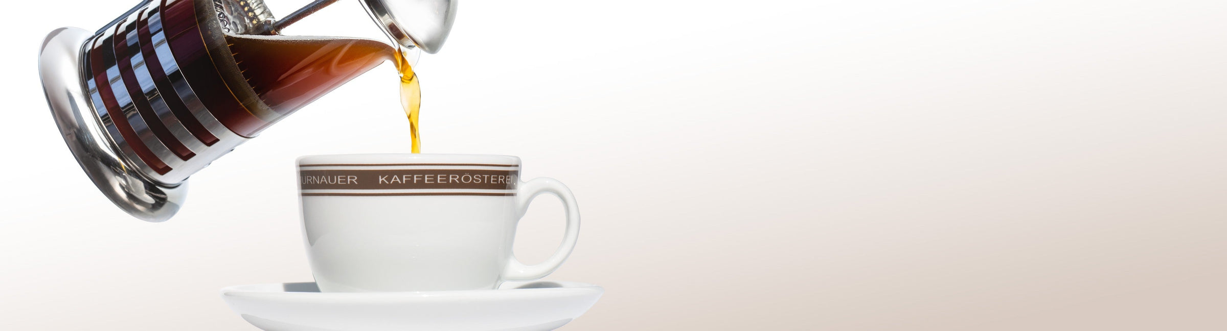 Frisch gebrühter Kaffee aus der French Press wird in eine Tasse der Murnauer Kaffeerösterei gegossen, helle Fläche rechts für Text, French Press KI erweitert mit Firefly Image 3