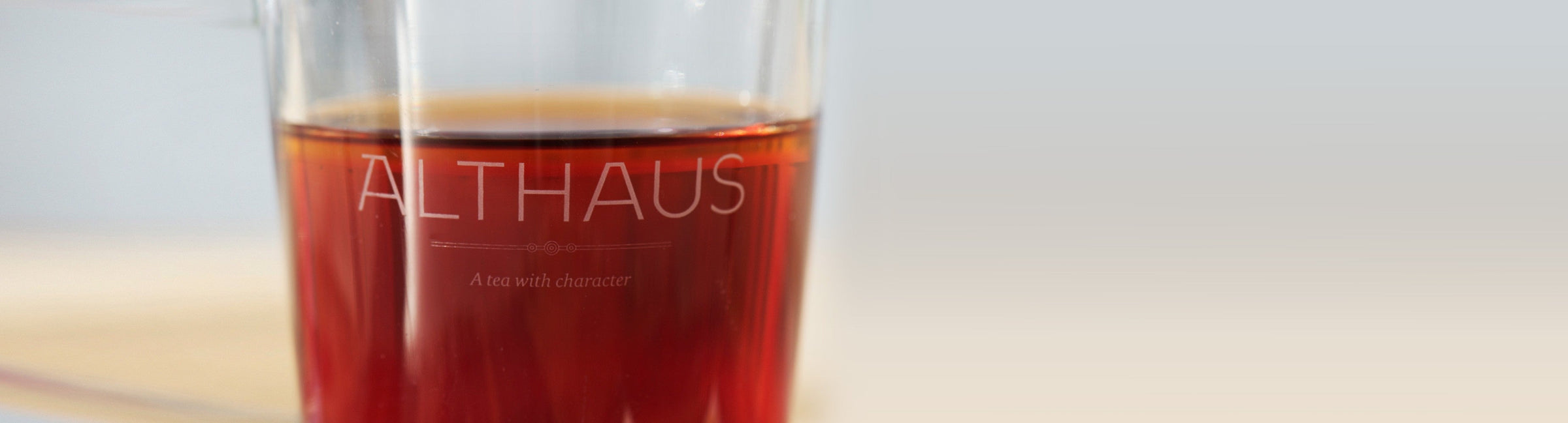 Nahaufnahme eines Glases mit dunklem Althaus Tee, links Logo auf Glas, rechts weicher Verlauf als Header