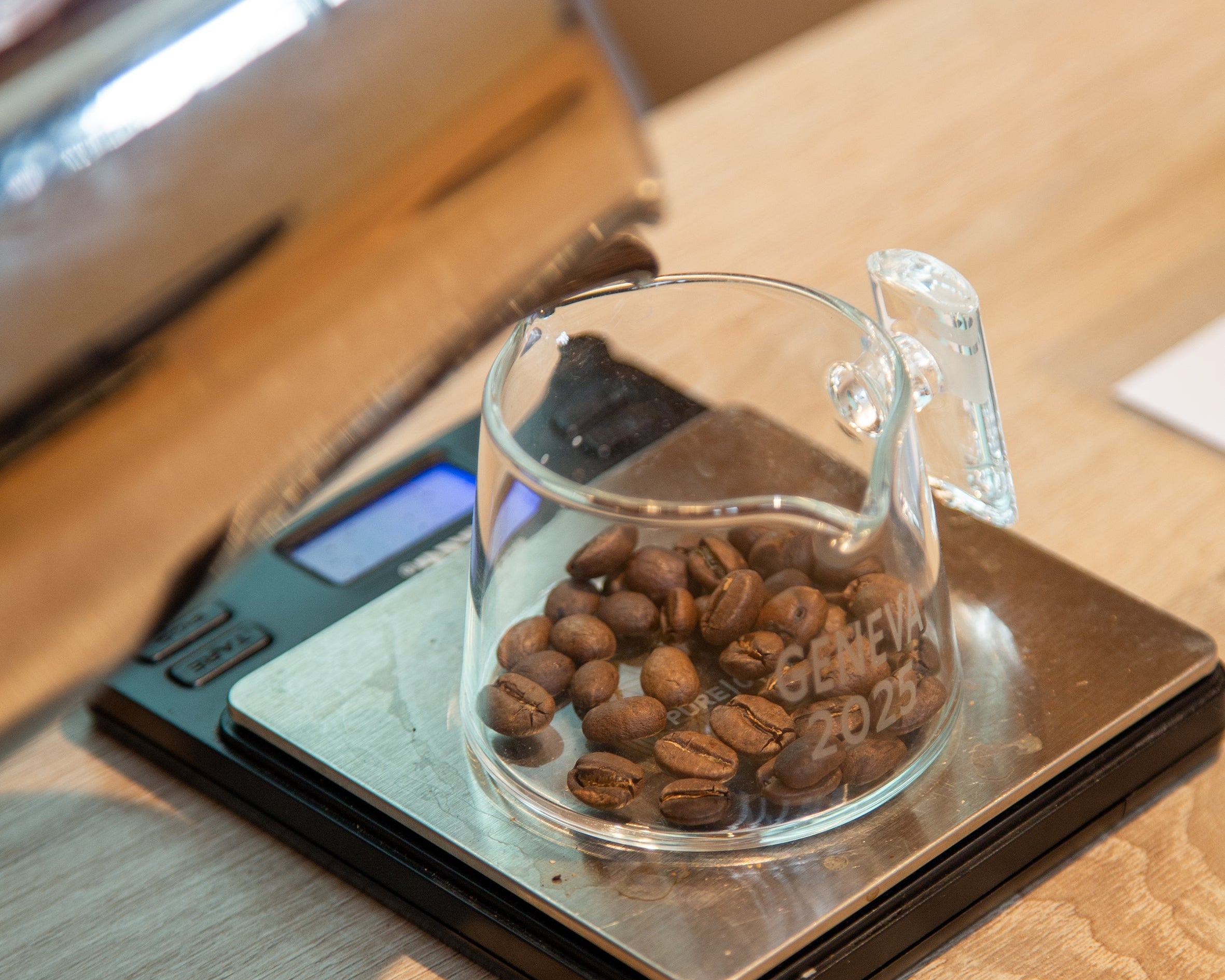 Kaffee-Kurs Brühen und Mahlen der Kaffee Academy im Murnauer Kaffeehaus: Kaffeebohnen im Glasgefäß auf Digitalwaage, Vorbereitung zum Brühen auf Holztisch