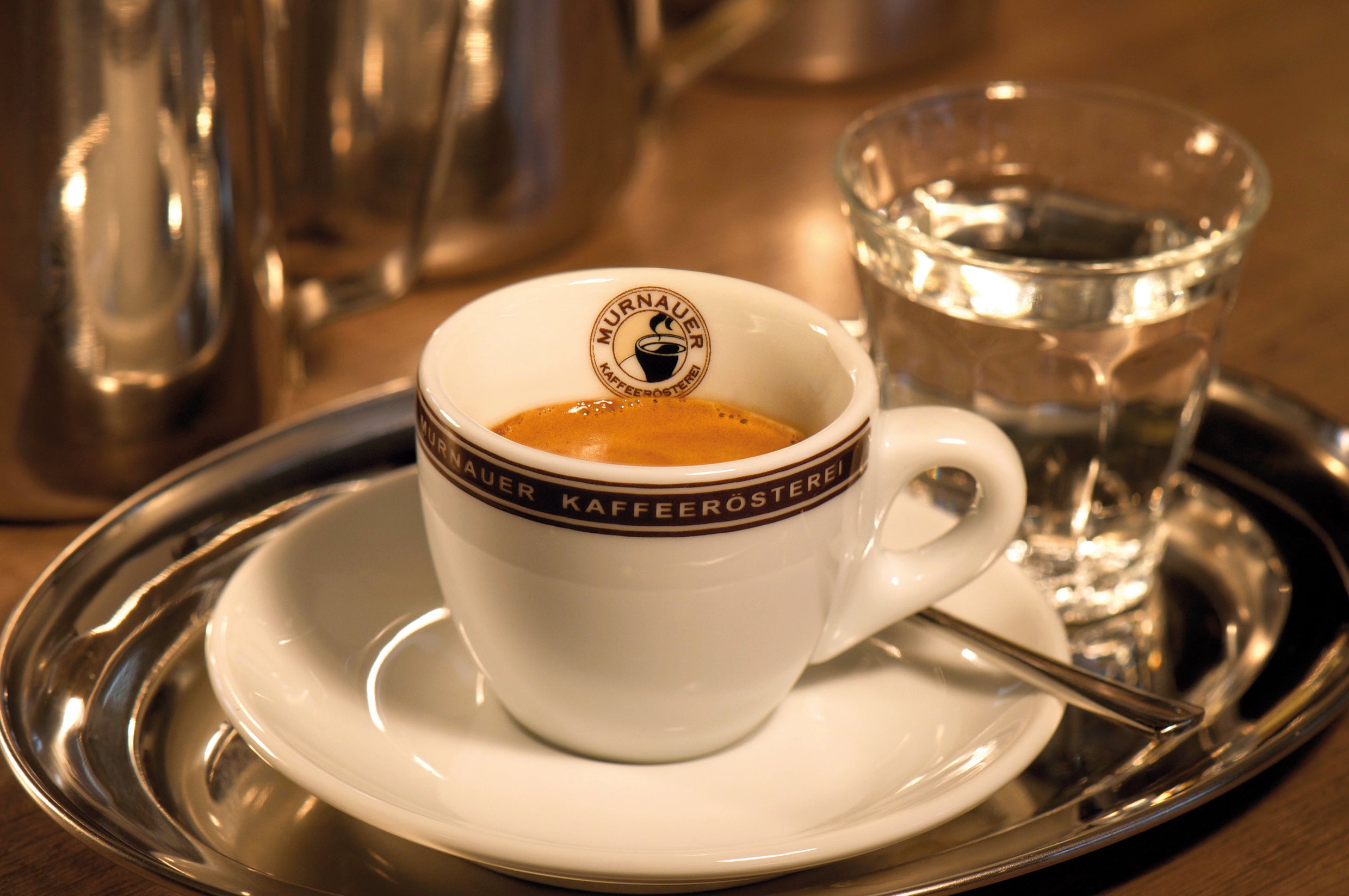 Espressotasse der Murnauer Kaffeerösterei auf Untertasse mit Löffel und Wasserglas auf silbernem Tablett im Kaffeehaus
