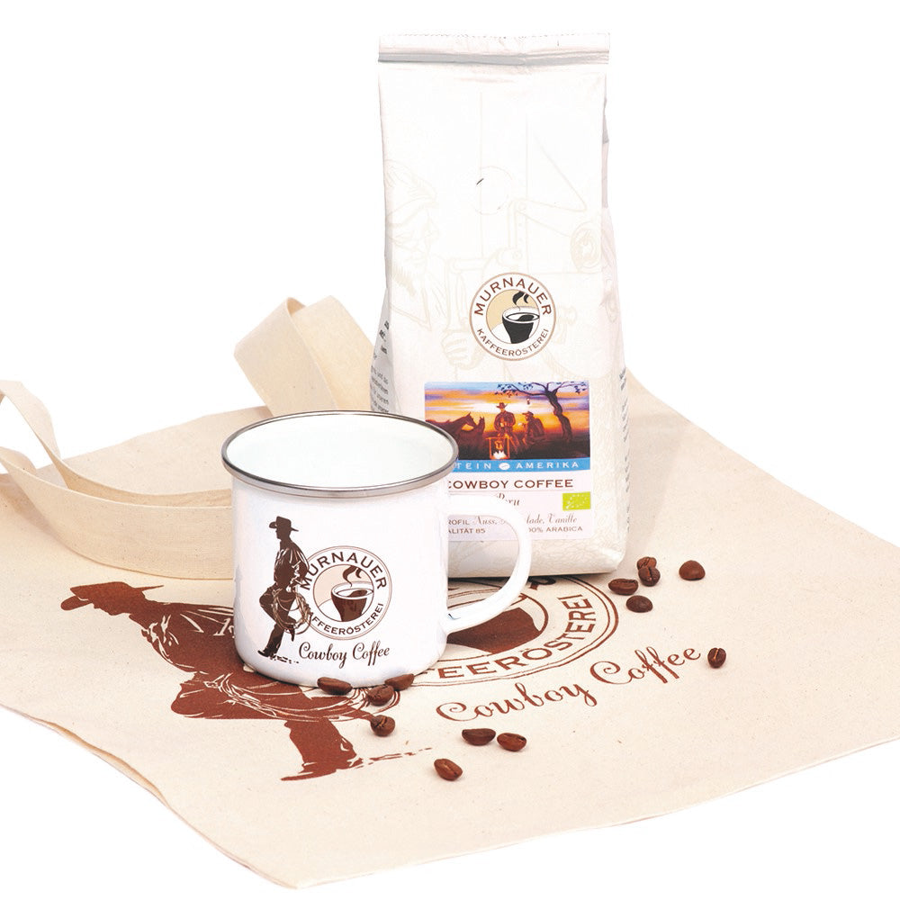 Geschenkset Cowboy Coffee frontal mit weißer Kaffeepackung, Emailletasse und bedruckter Baumwolltasche der Murnauer Kaffeerösterei, Bohnen auf dem Stoff