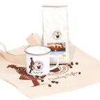Geschenkset Cowboy Coffee frontal mit weißer Kaffeepackung, Emailletasse und bedruckter Baumwolltasche der Murnauer Kaffeerösterei, Bohnen auf dem Stoff