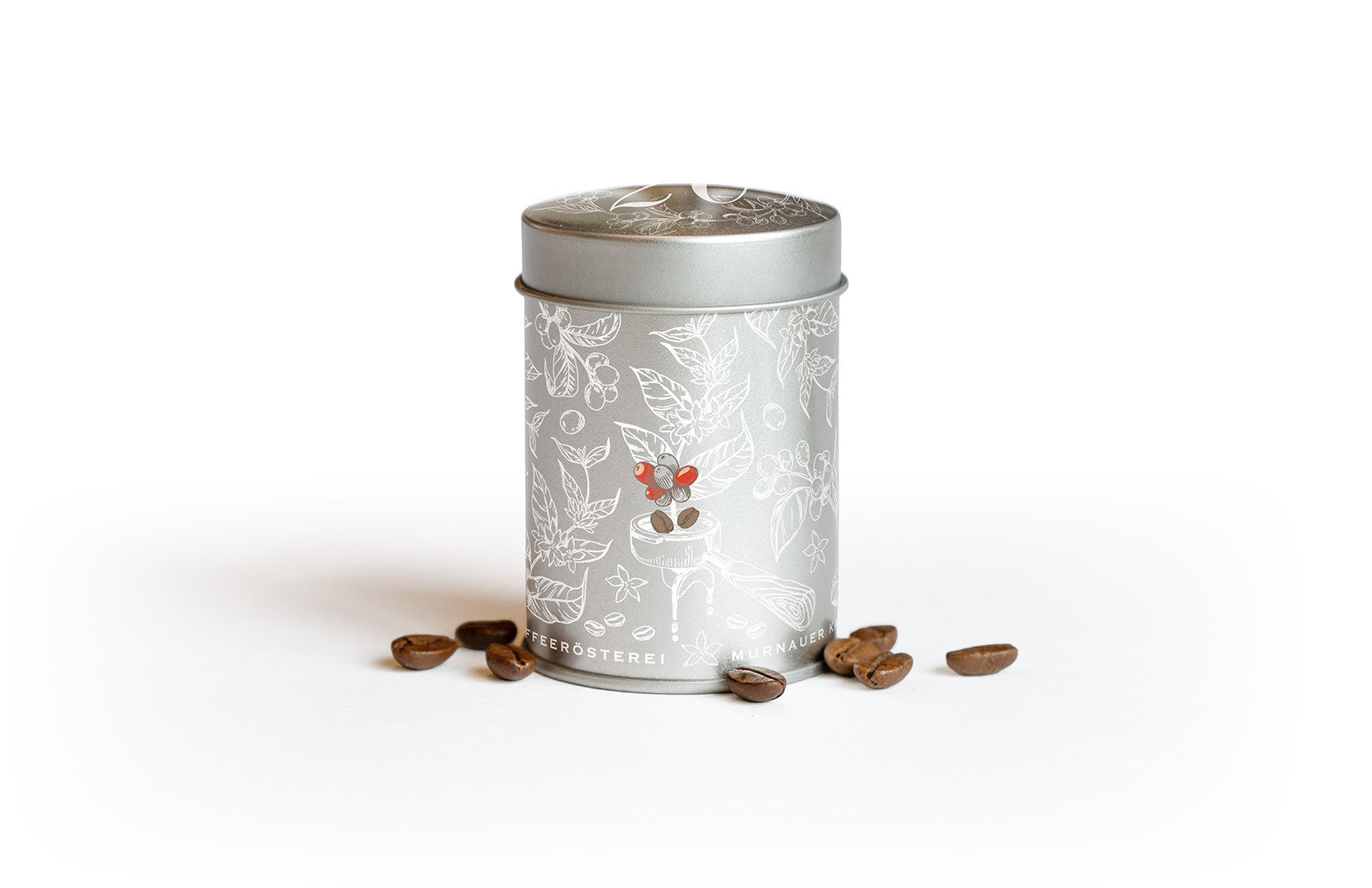 Silberne Kaffeeblechdose aus dem Kaffee-Adventskalender 2026 der Murnauer Kaffeerösterei, umgeben von einzelnen Kaffeebohnen vor weißem Hintergrund