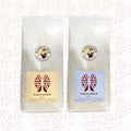 Zwei weiße Kaffeepackungen als Aromareise Aquiares Costa Rica Set der Murnauer Kaffeerösterei vor dezent gemustertem Hintergrund