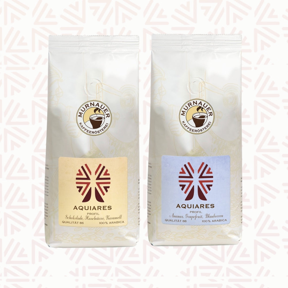 Zwei weiße Kaffeepackungen als Aromareise Aquiares Costa Rica Set der Murnauer Kaffeerösterei vor dezent gemustertem Hintergrund