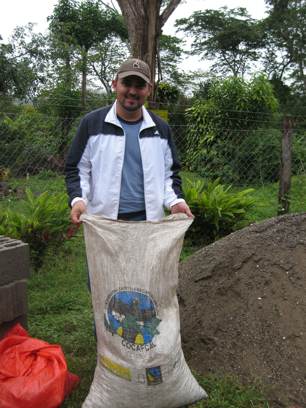 Kaffeebauer der COCAFCAL Kooperative hält vollen Sack Bella Vista Honduras Kaffee vor grüner Vegetation in Las Capucas