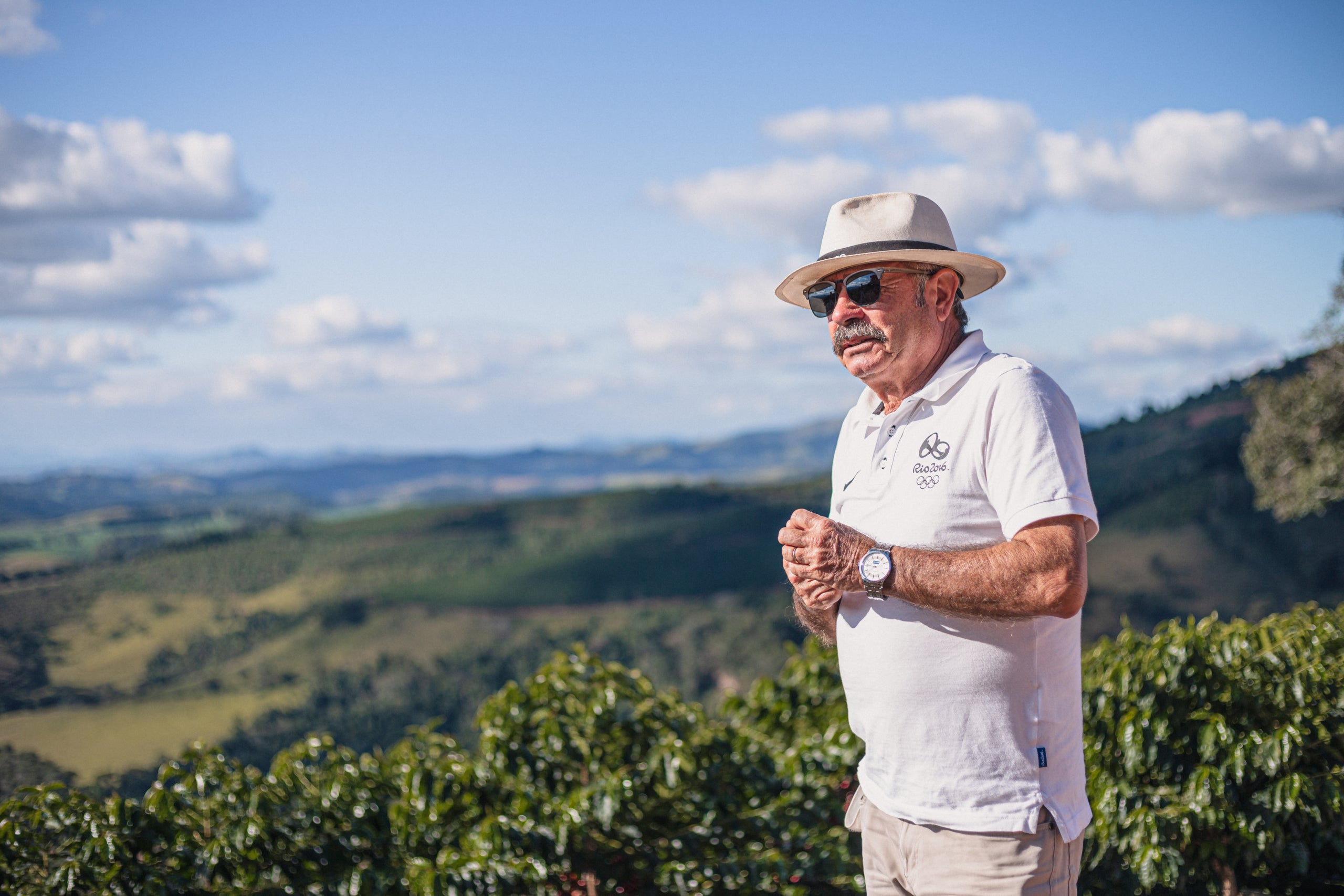 Produzent auf der Fazenda Rainha Brasilien Kaffeeplantage mit Hut und Sonnenbrille steht vor grünem Hügelland unter blauem Himmel