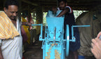 Zwei Arbeiter verarbeiten Jamala Indien Bio Robusta Kaffee in blauer Aufbereitungsmaschine, helle Kaffeebohnen laufen vorne heraus