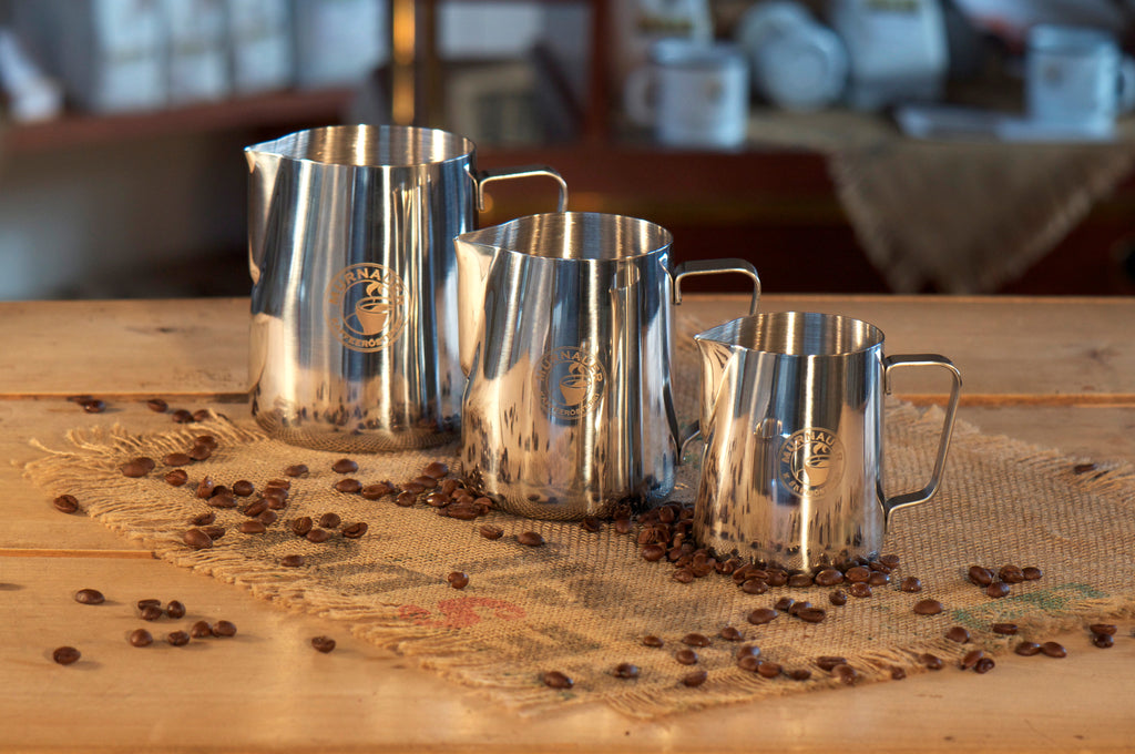 Drei Edelstahl Milchkännchen der Murnauer Kaffeerösterei in verschiedenen Größen stehen auf Jutesack mit verstreuten Kaffeebohnen, 350 ml, 590 ml, 950 ml