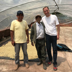 Drei Männer stehen im Trocknungszelt der Association Miguel Grau vor hellen Pergamentkaffeebohnen für das Pacha Mama BIO‑Projekt in Peru