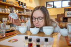  Teilnehmerin im Kaffeesensorik Kurs der Kaffee Academy im Murnauer Kaffeehaus riecht an weißen Cupping-Tassen auf Holztisch