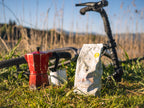 Kaffeelust Wadelpause Kaffee im Beutel mit roter Mokkakanne und Tasse auf Wiese neben Fahrradlenker in der Sonne