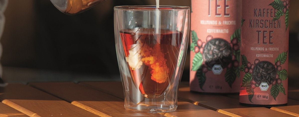 Glas mit roter Fluessigkeit Cascara, in die Milch gegossen wird