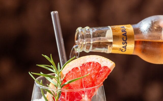 La Cascara Spritz - ReadyTo Drink - Das Produkt wird aus der Flasche in ein Glas mit Rosmarin und Grapefruit eingegossen