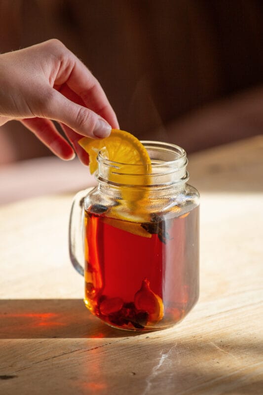 Cascara Punsch wird mit Orangenscheibe garniert und steht auf einem holztisch