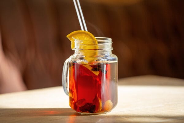 Cascara punsch mit orange garniert in glas auf einem holztisch von der sonne angestrahlt