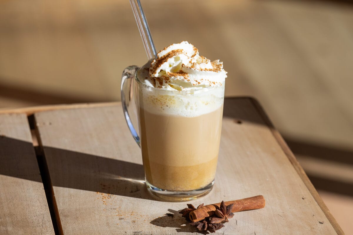 pumpkin spice latte mit sahne und zimt bestreut mit glasstrohhalm umd zimtstange und sternanis als Deko auf holztisch