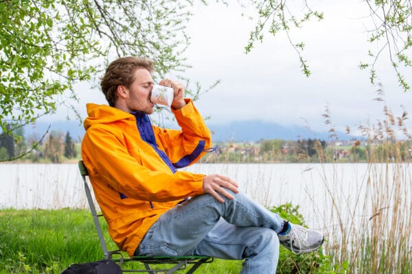 draußen kaffee trinken: mann trinkt sitzt inm stuhl draussen am see einen kaffee aus einer emailletasse