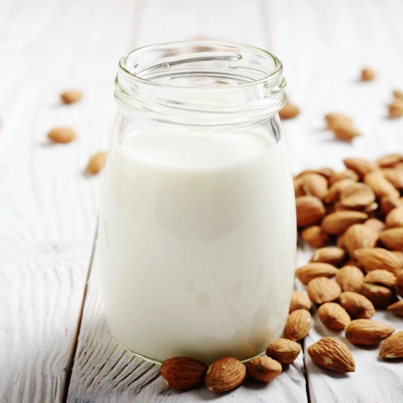 Milk or yogurt in mason jar on white wooden table with almonds a